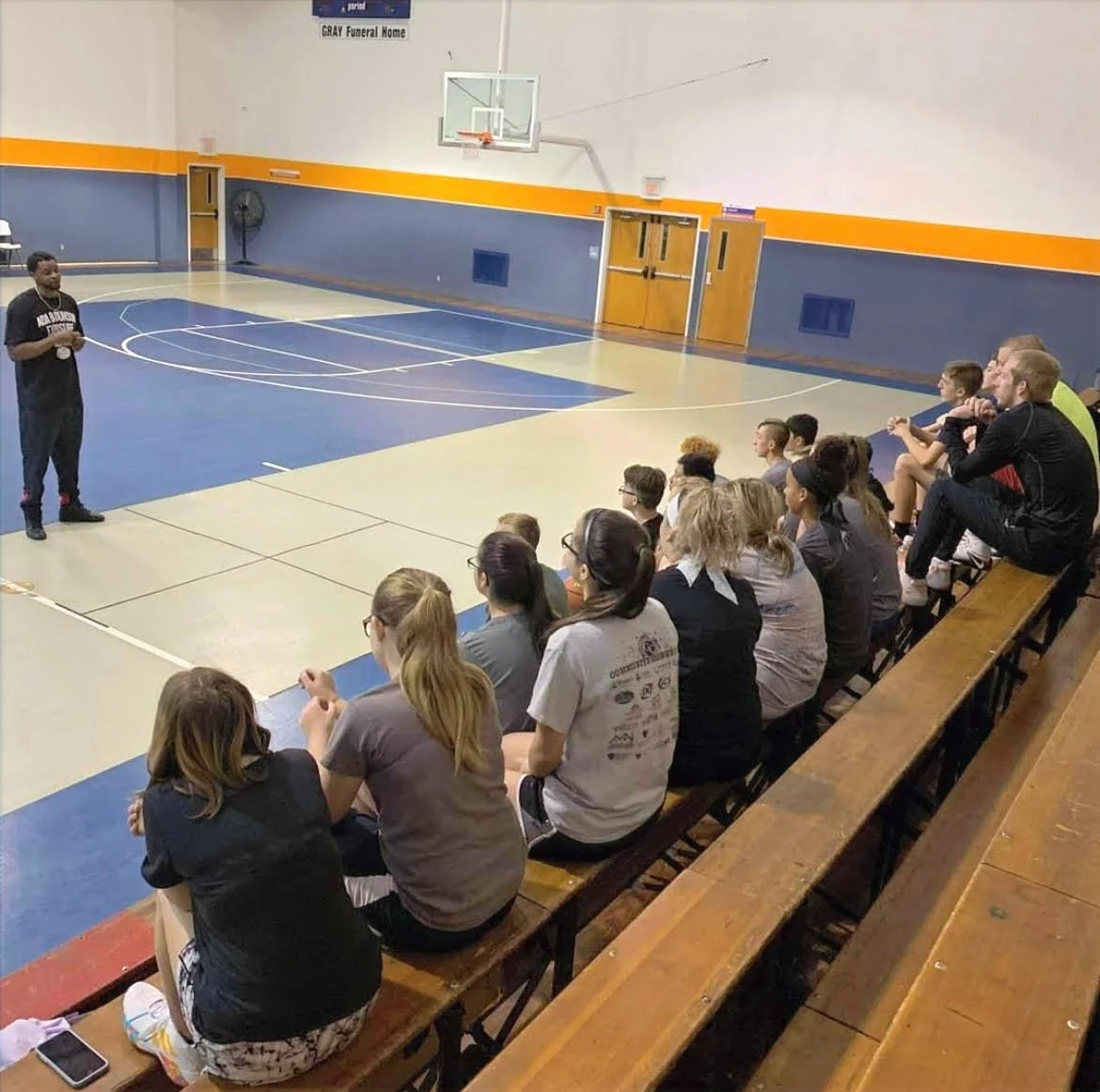 Coach Riggs addressing a group of students seated in a gym